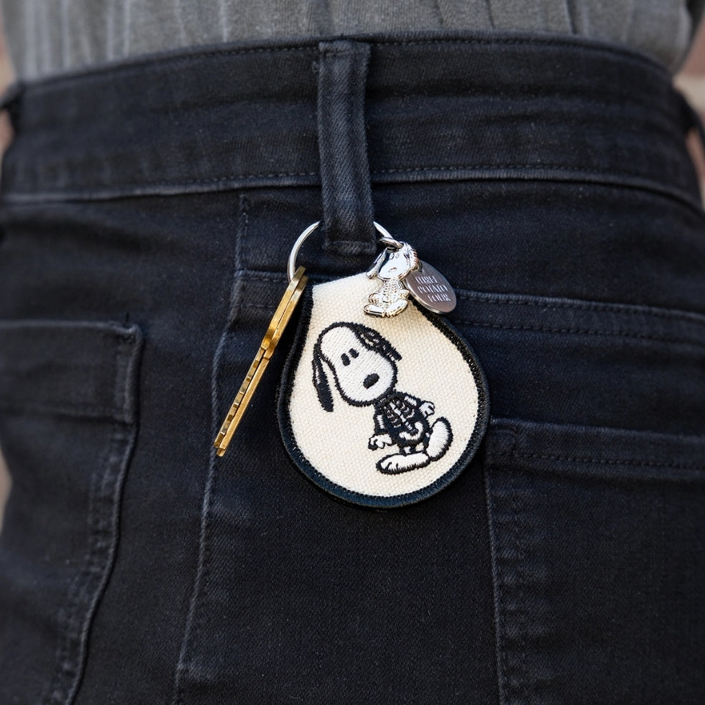 Snoopy Skeleton patch keychain clipped to the belt loop of black jeans with a brass key